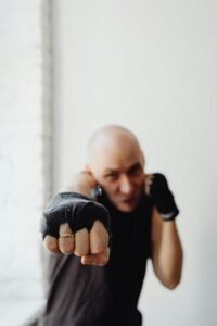 Dynamic portrait of a bald boxer delivering a punch with a blurred background, indoors.
