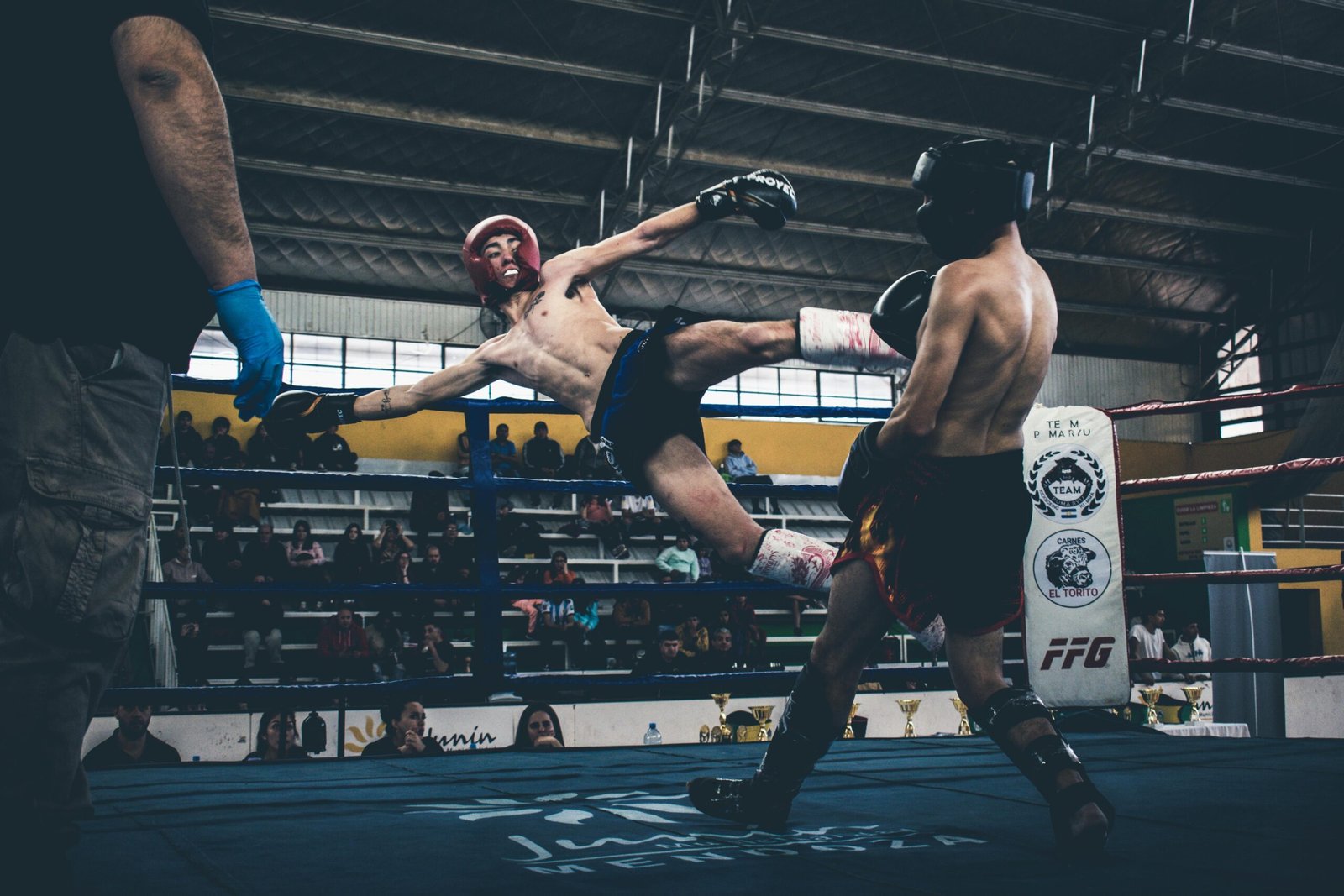 High-energy kickboxing match showcasing powerful move with attentive spectators in an indoor arena.