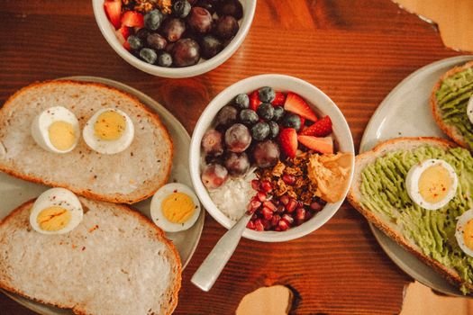 A fresh and vibrant breakfast flat lay featuring a yogurt bowl with fruits and toast with eggs and avocado.