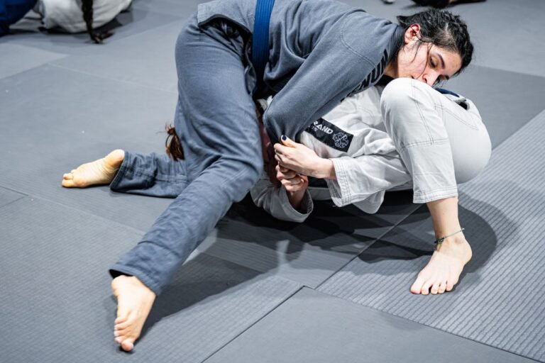 Two women practicing Jiu-Jitsu, demonstrating grappling techniques indoors.